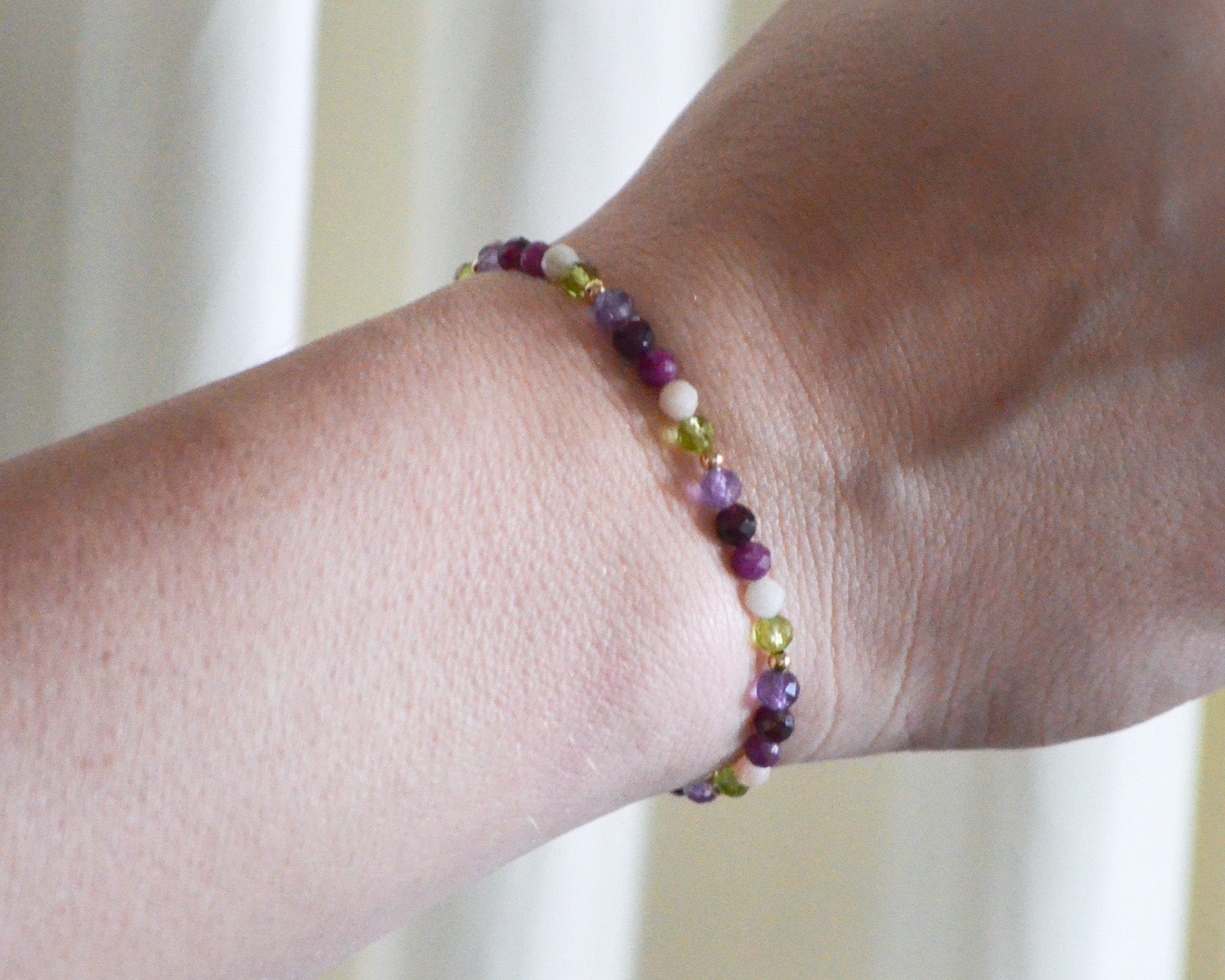 Multicolored beaded birthstone bracelet on a wrist with a blurred background