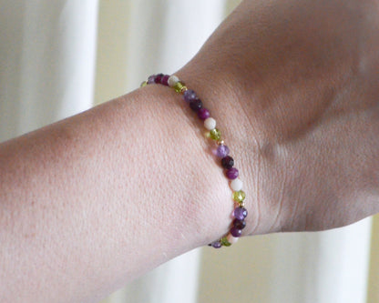 Multicolored beaded birthstone bracelet on a wrist with a blurred background