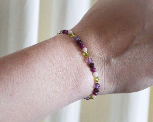Multicolored beaded birthstone bracelet on a wrist with a blurred background