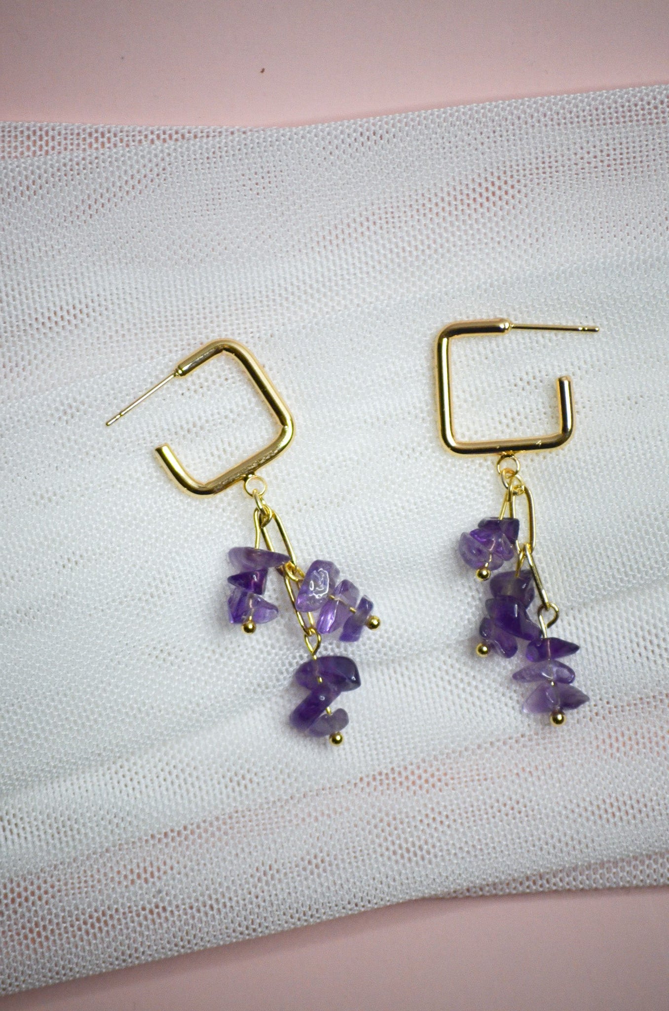 Gold earrings with purple stones on a textured white surface