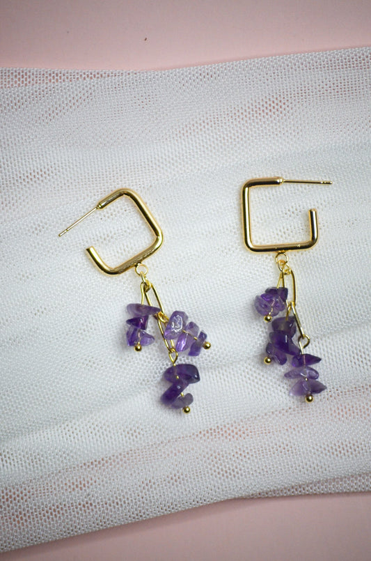 Gold earrings with purple stones on a textured white surface