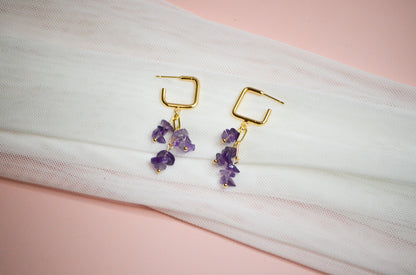 Gold earrings with purple gemstones on a white and pink fabric background