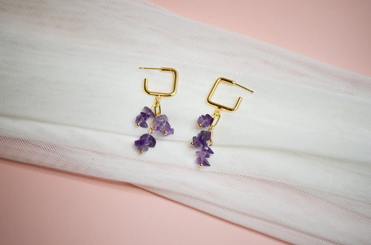Gold earrings with purple gemstones on a white and pink fabric background