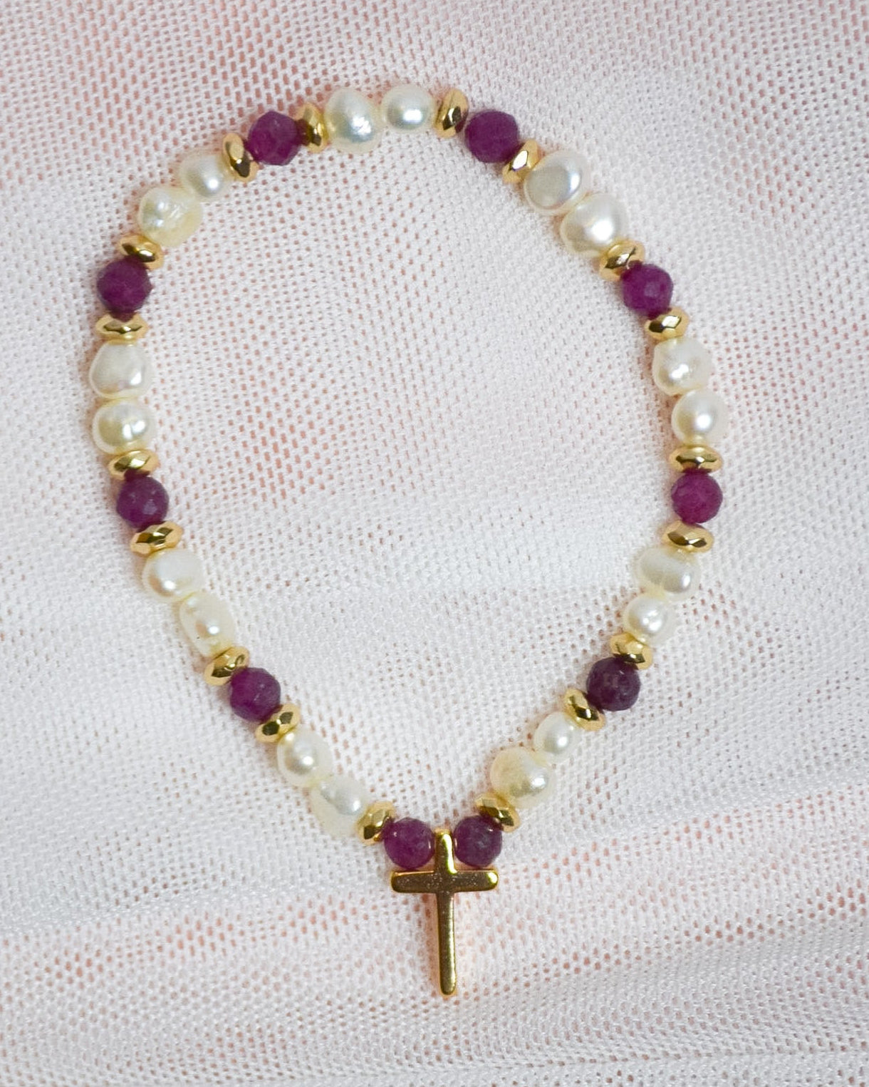 Bracelet with purple, gold, and pearl beads on a light pink fabric background