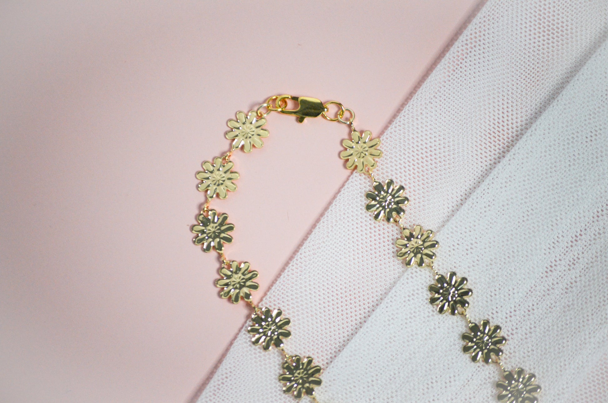 Gold necklace with floral designs on a light pink and white background