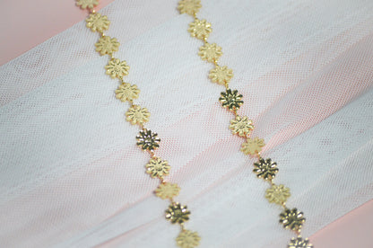 Gold floral necklace on a light pink fabric background