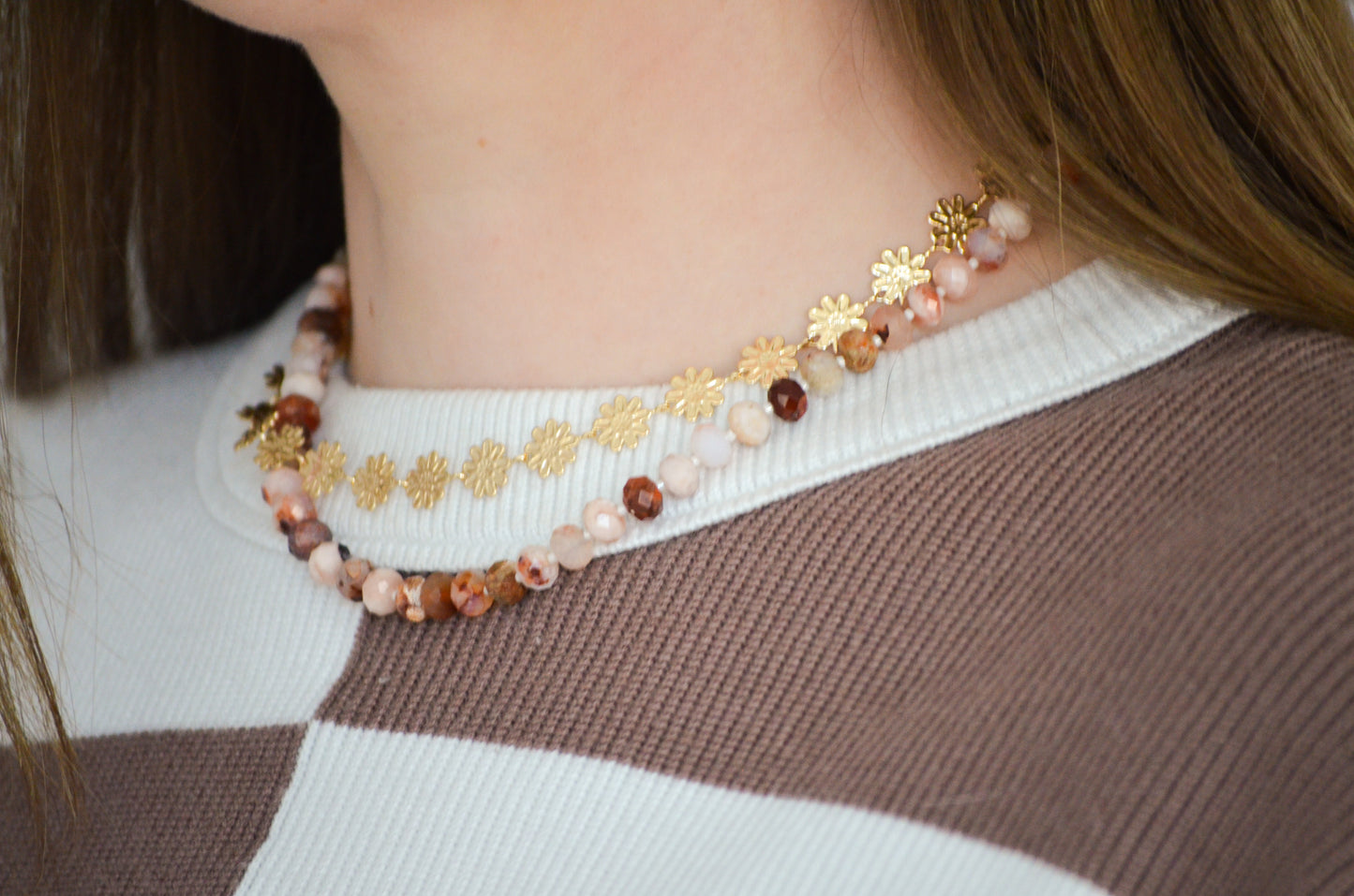 Gold floral necklac epaired with a beaded necklace on a woman with a brown and white sweter
