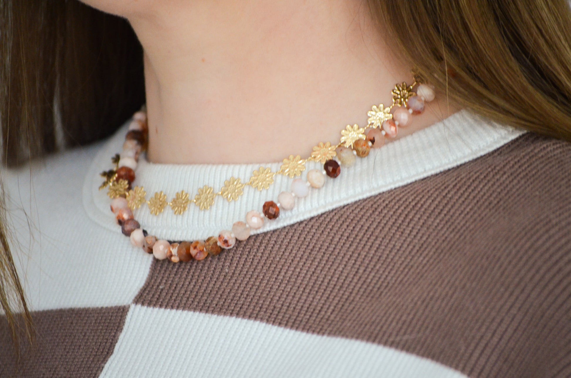 Gold floral necklac epaired with a beaded necklace on a woman with a brown and white sweter