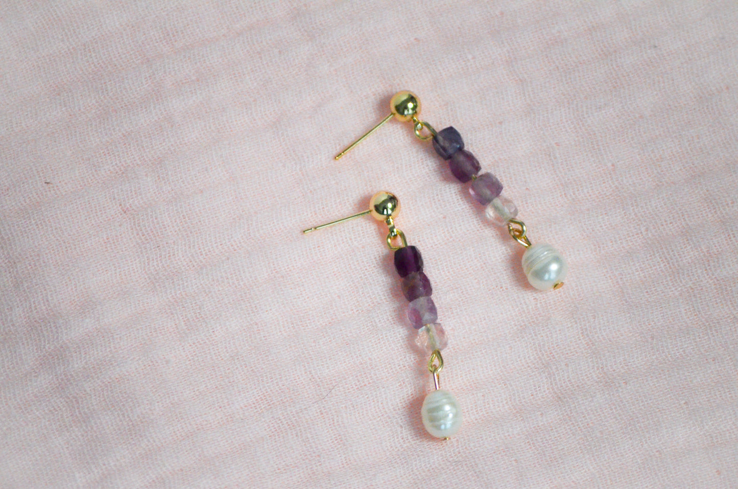 Pair of gold, purple gemstone, and pearl beaded earrings on a pink background