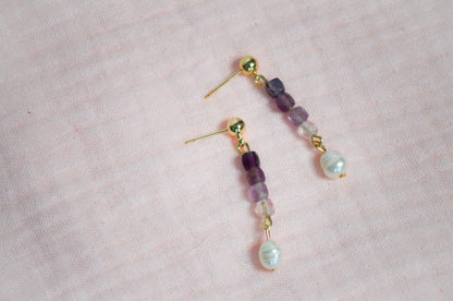 Pair of gold, purple gemstone, and pearl beaded earrings on a pink background