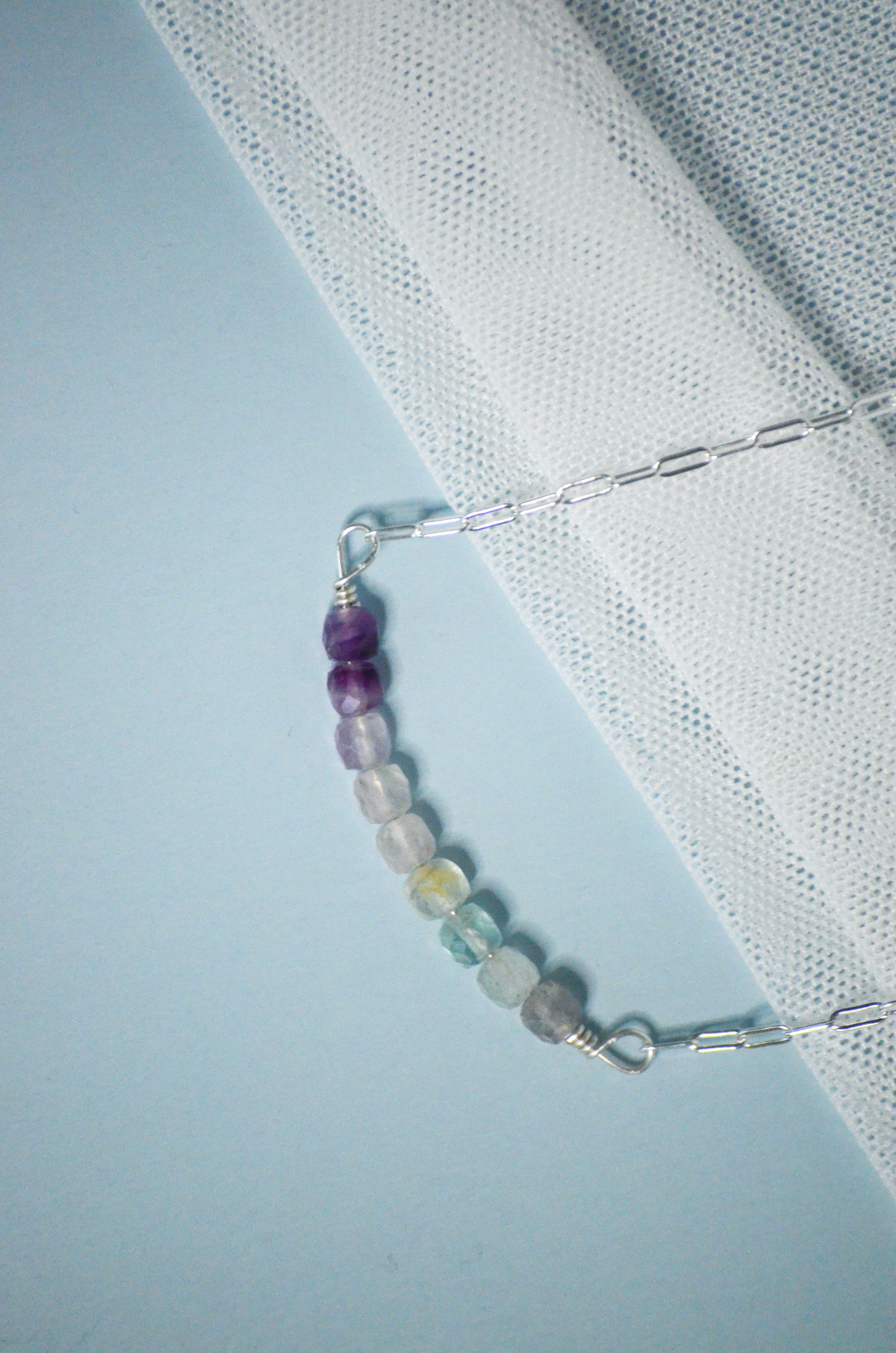 Silver chain necklace with multicolored beads on a light blue background