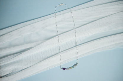 Silver chain necklace with colorful beads on a light blue background