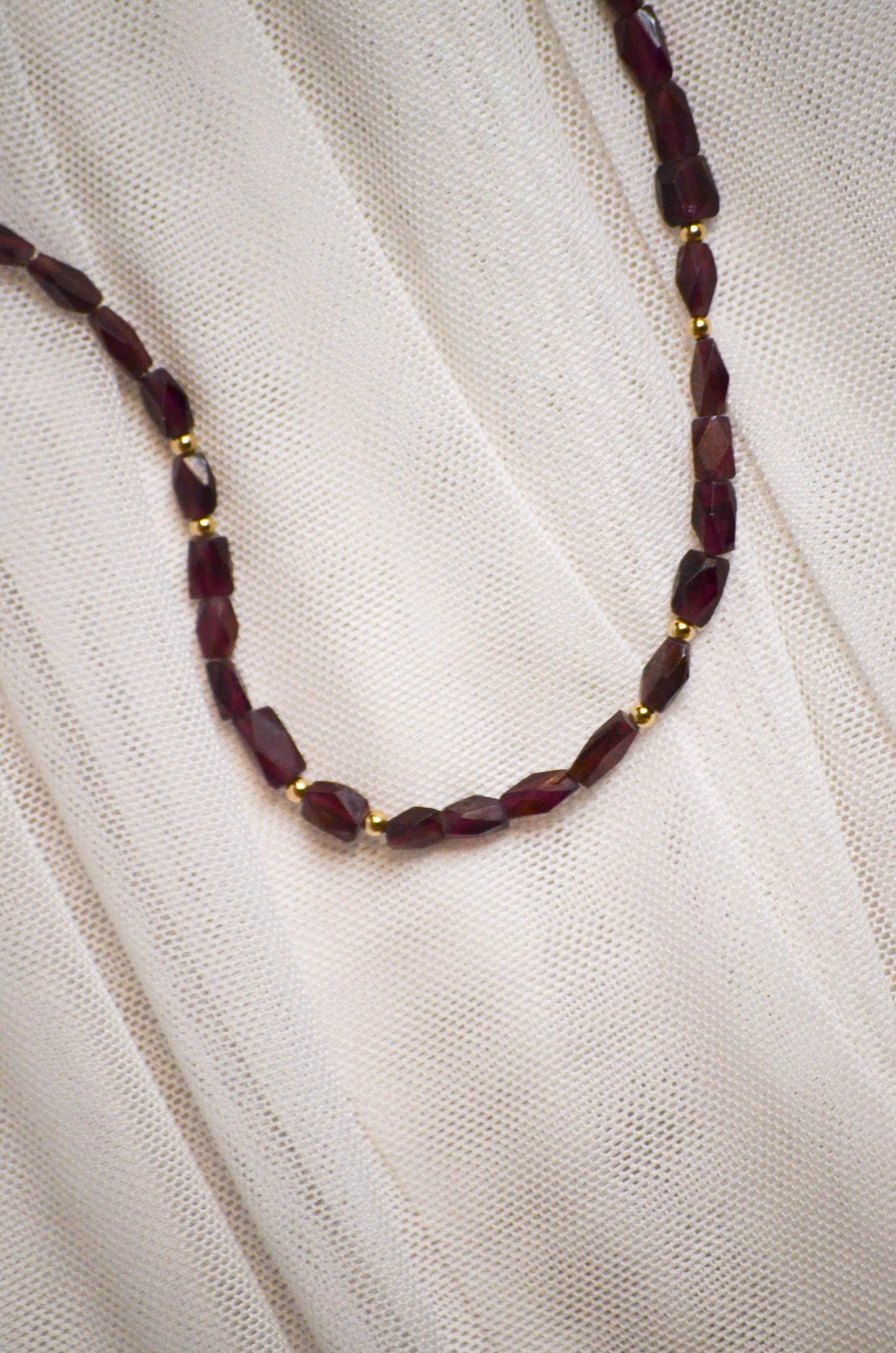Necklace with burgundy and gold beads on a white fabric background.