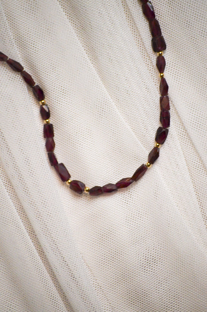 Necklace with burgundy and gold beads on a white fabric background.