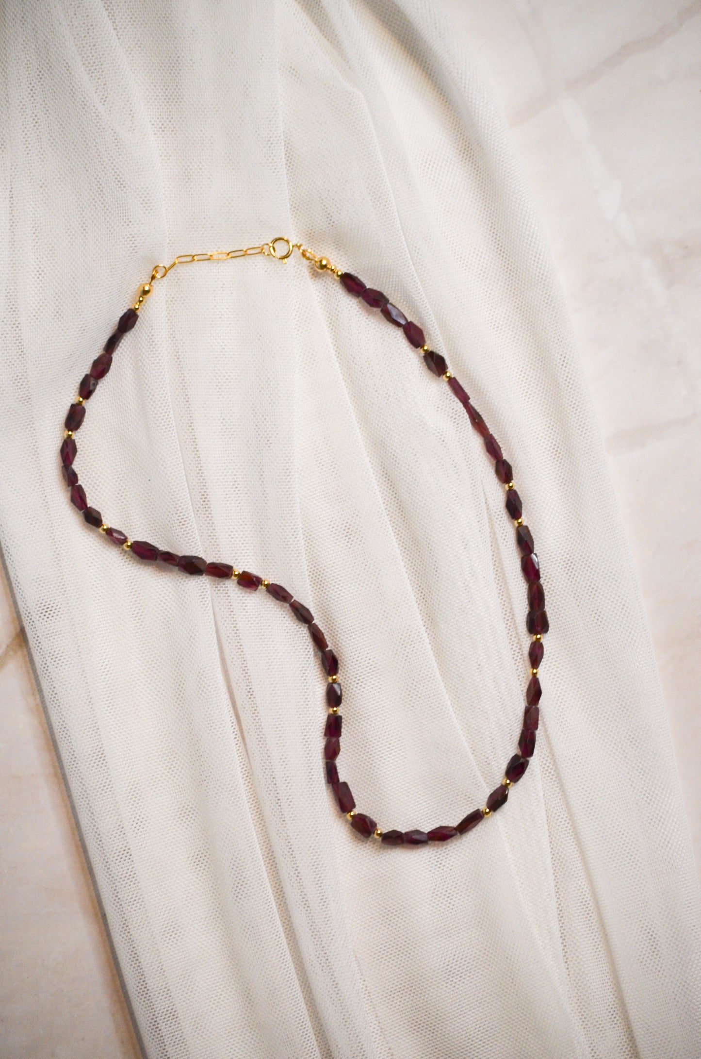 Necklace with burgundy and beads and gold clasp on a white fabric background