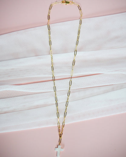 Gold chain necklace with a cross pendant on a pink background