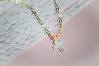 Gold chain necklace with a cross pendant on a pink and white textured background