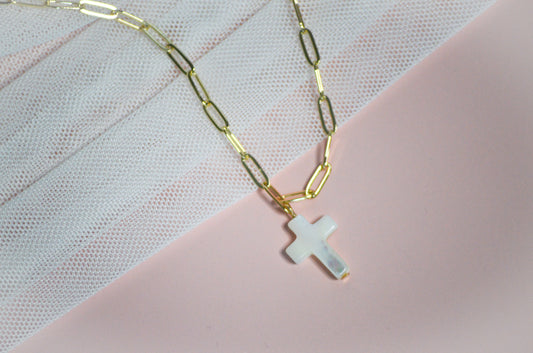 Gold chain necklace with a cross pendant on a pink and white textured background
