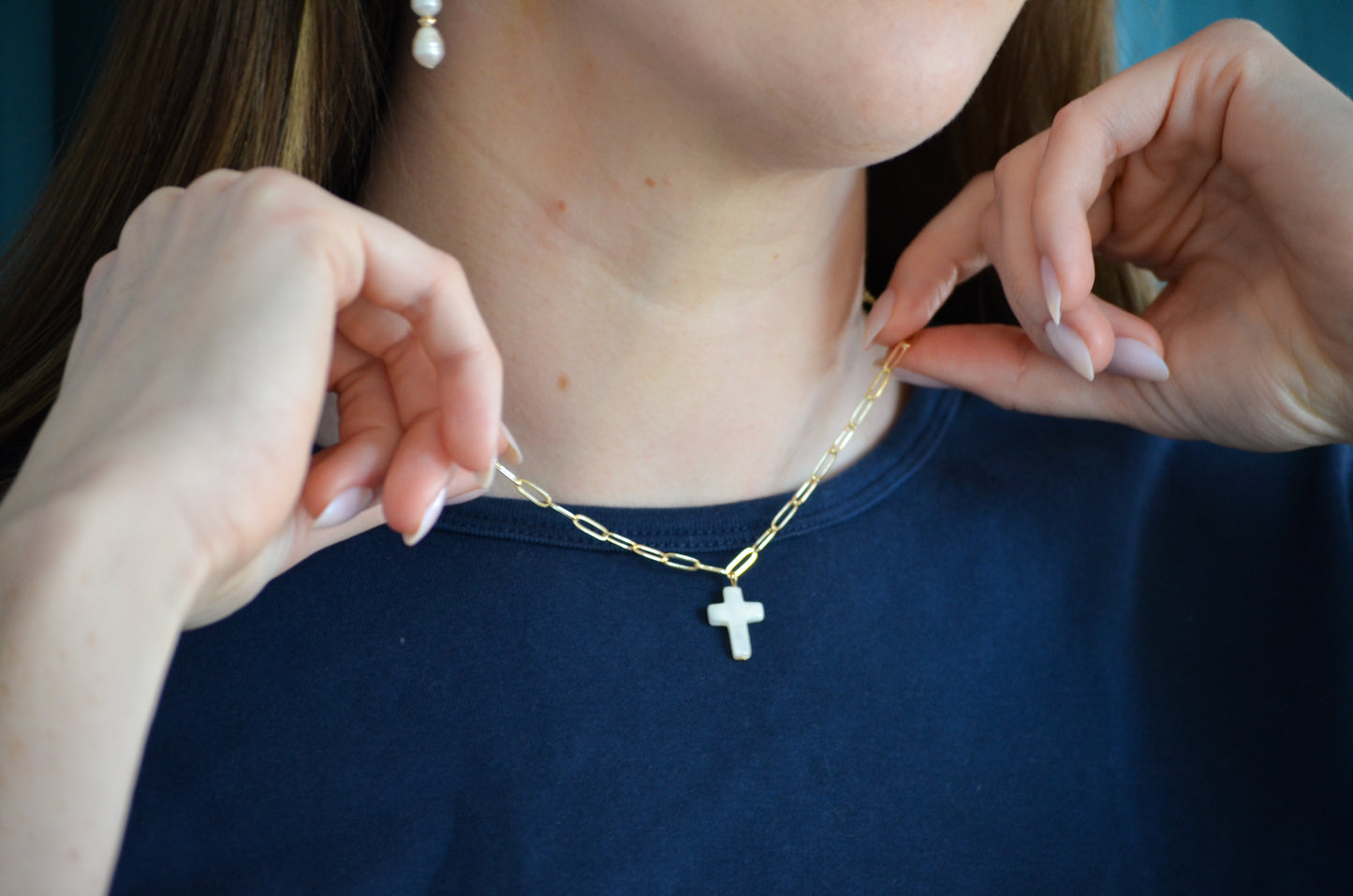Person wearing a gold necklace with a cross pendant, held by another person.