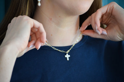 Person wearing a gold necklace with a cross pendant, held by another person.