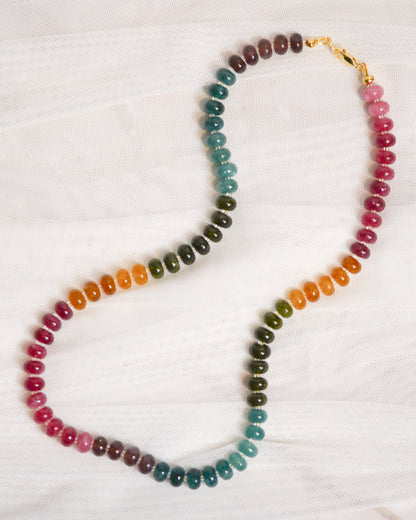 Multicolored beaded necklace with a gold clasp on a white fabric background