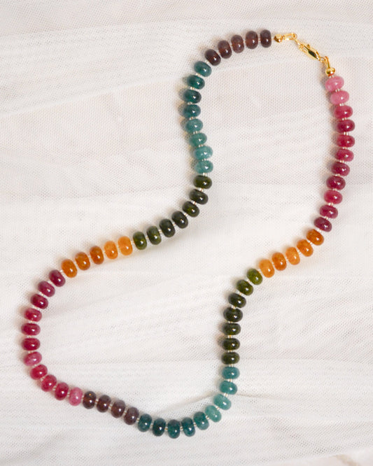 Multicolored beaded necklace with a gold clasp on a white fabric background