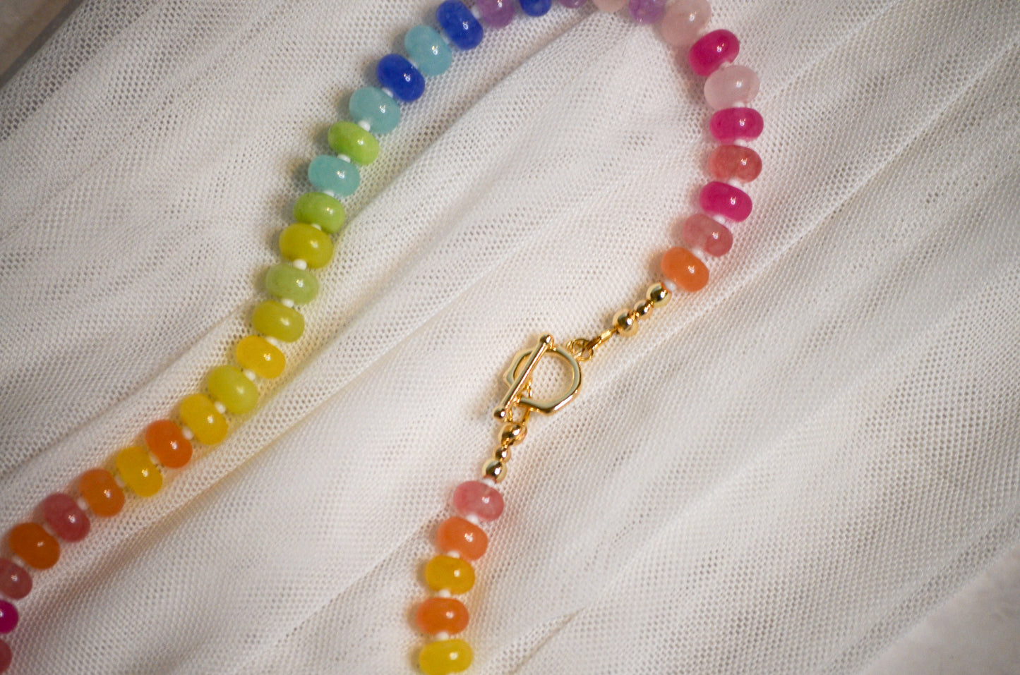 Colorful beaded necklace with a gold toggle clasp on a white fabric background