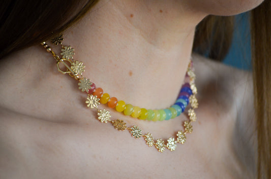 Close-up of a person wearing two necklaces with floral and rainbow beaded designs.