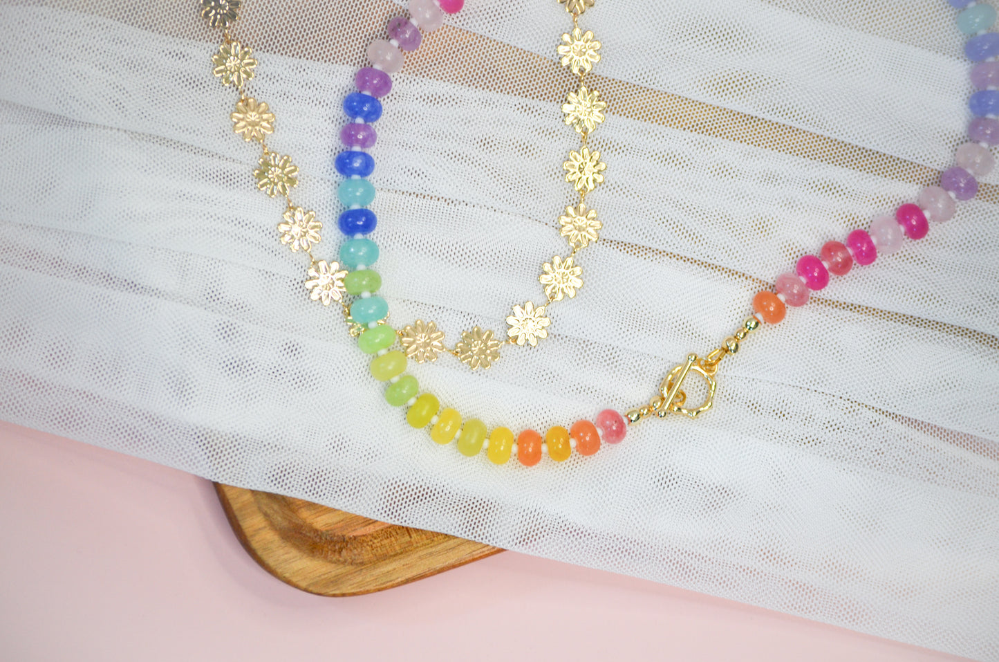 Colorful beaded necklace and gold flower chain necklace on a white fabric background