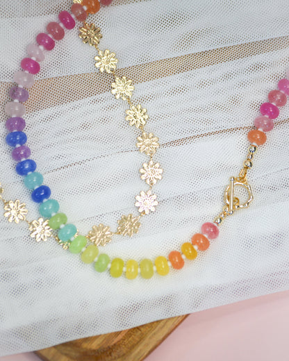 Colorful beaded necklace and gold flower chain necklace on a white fabric background