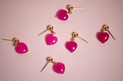 Heart-shaped pink earrings with gold accents on a pink background