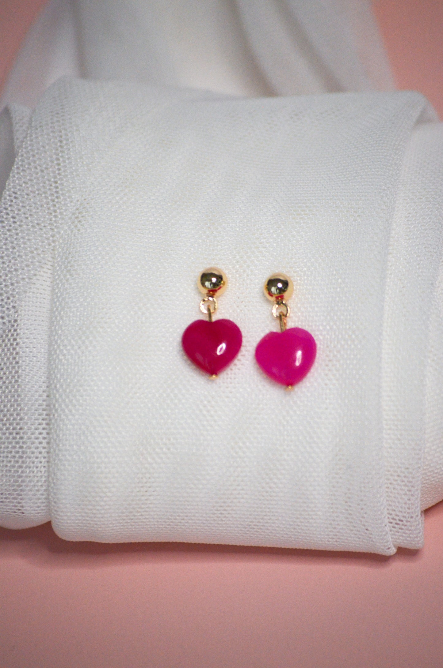 Pink heart-shaped dangle earrings on a white fabric background