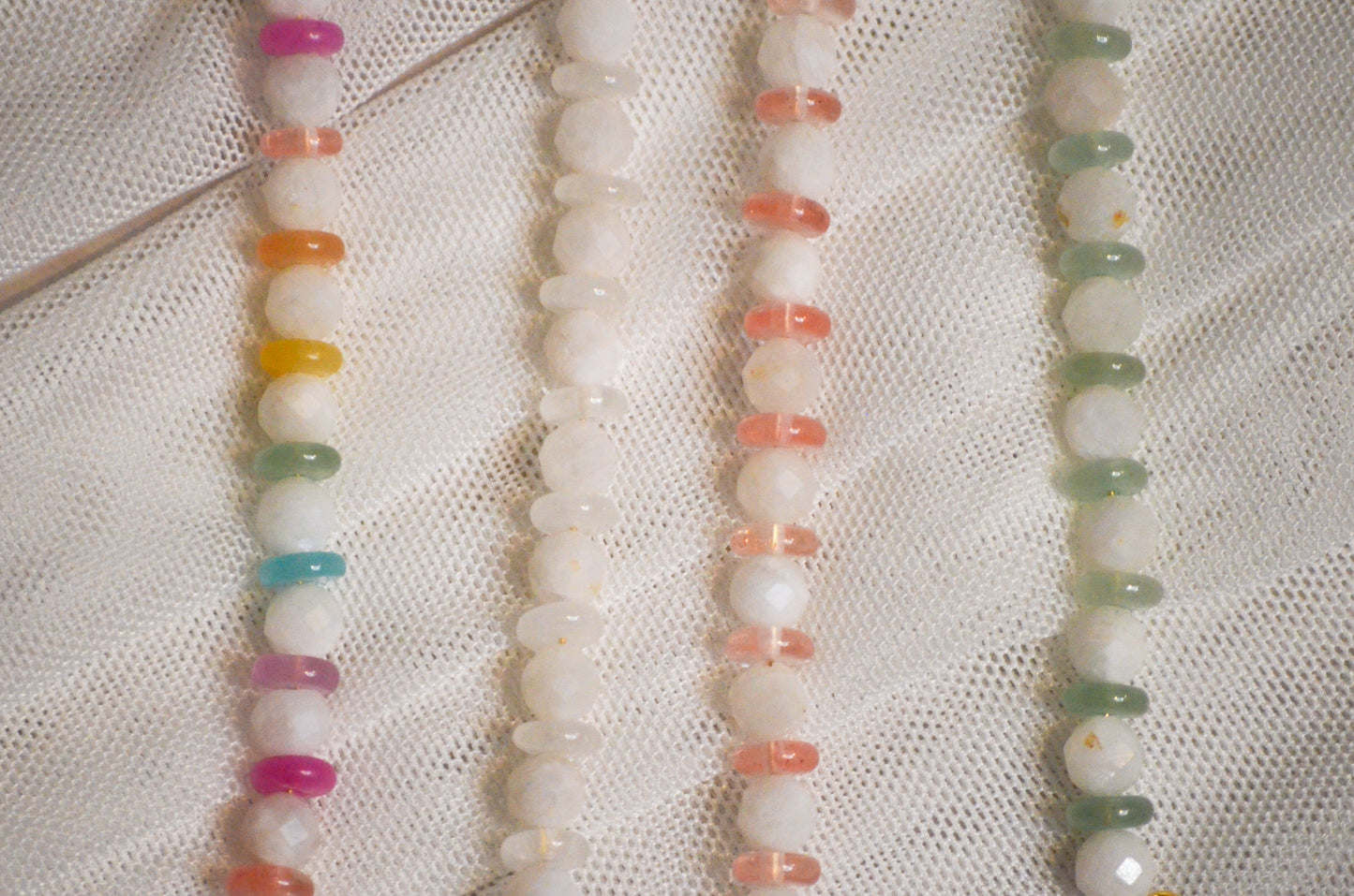 Four strands of multicolored beads on a white fabric background