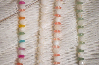 Four strands of multicolored beads on a white fabric background