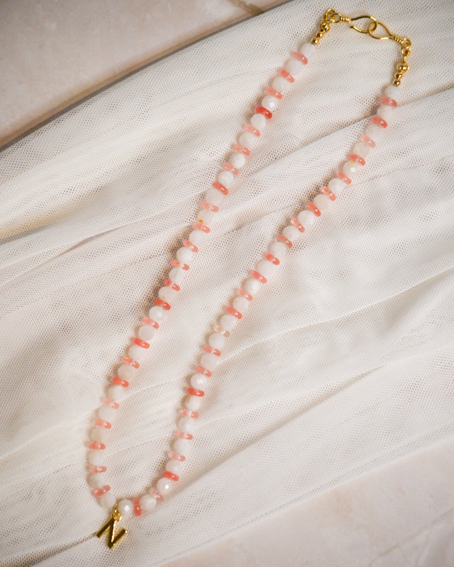 Peach and white beaded necklace with gold clasp on a light fabric background