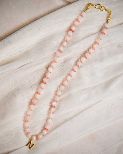 Peach and white beaded necklace with gold clasp on a light fabric background