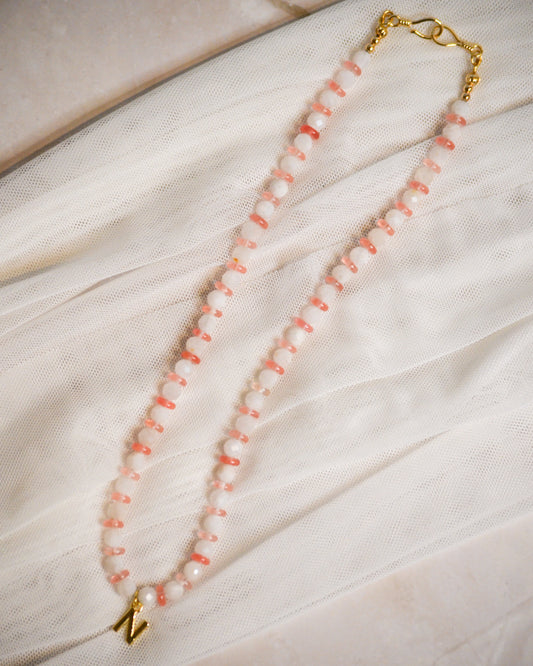 Peach and white beaded necklace with gold clasp on a light fabric background