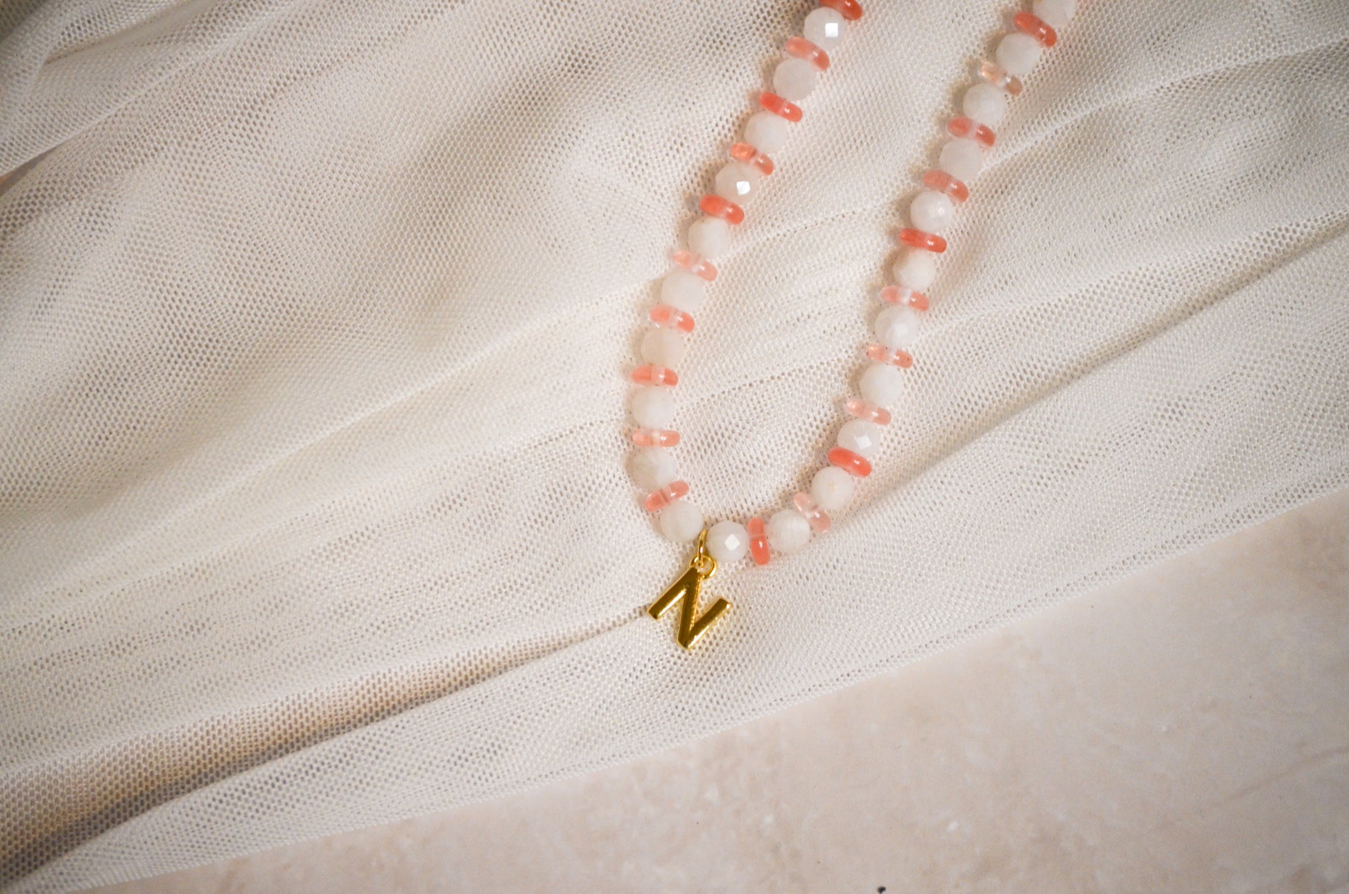 Necklace with pink beads and a gold charm on a light fabric background