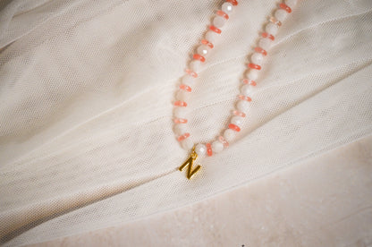 Necklace with pink beads and a gold charm on a light fabric background