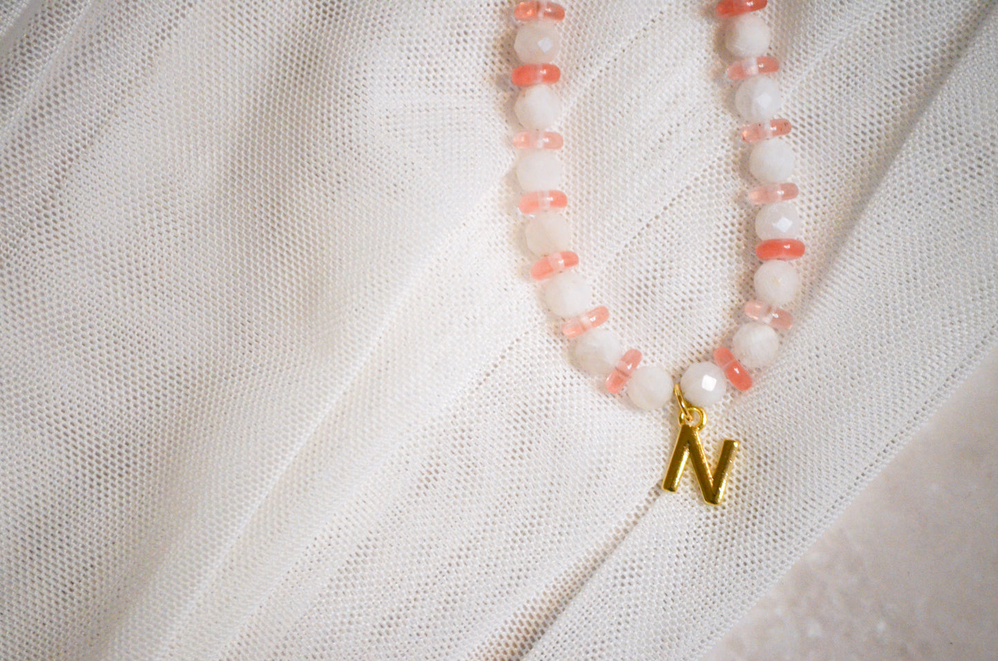 Necklace with pink beads and a gold pendant on a white fabric background