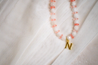 Necklace with pink beads and a gold pendant on a white fabric background