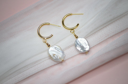 Gold hoop earrings with organic shaped pearl beads on a light fabric background
