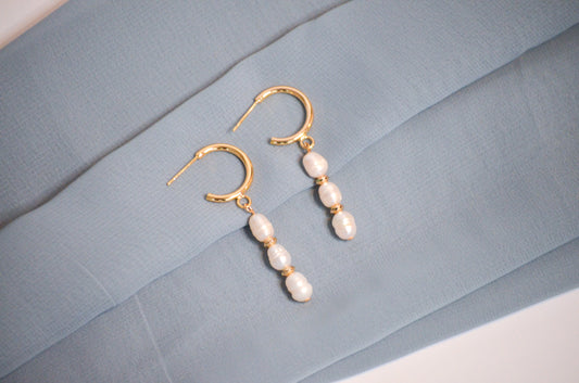 Pearl earrings with gold hooks on a light blue fabric background