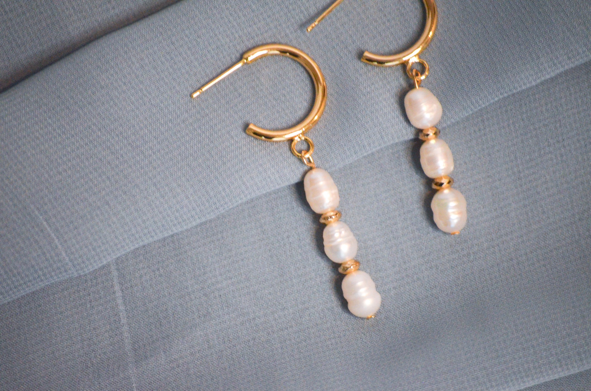Pearl earrings with gold hooks on a gray textured surface