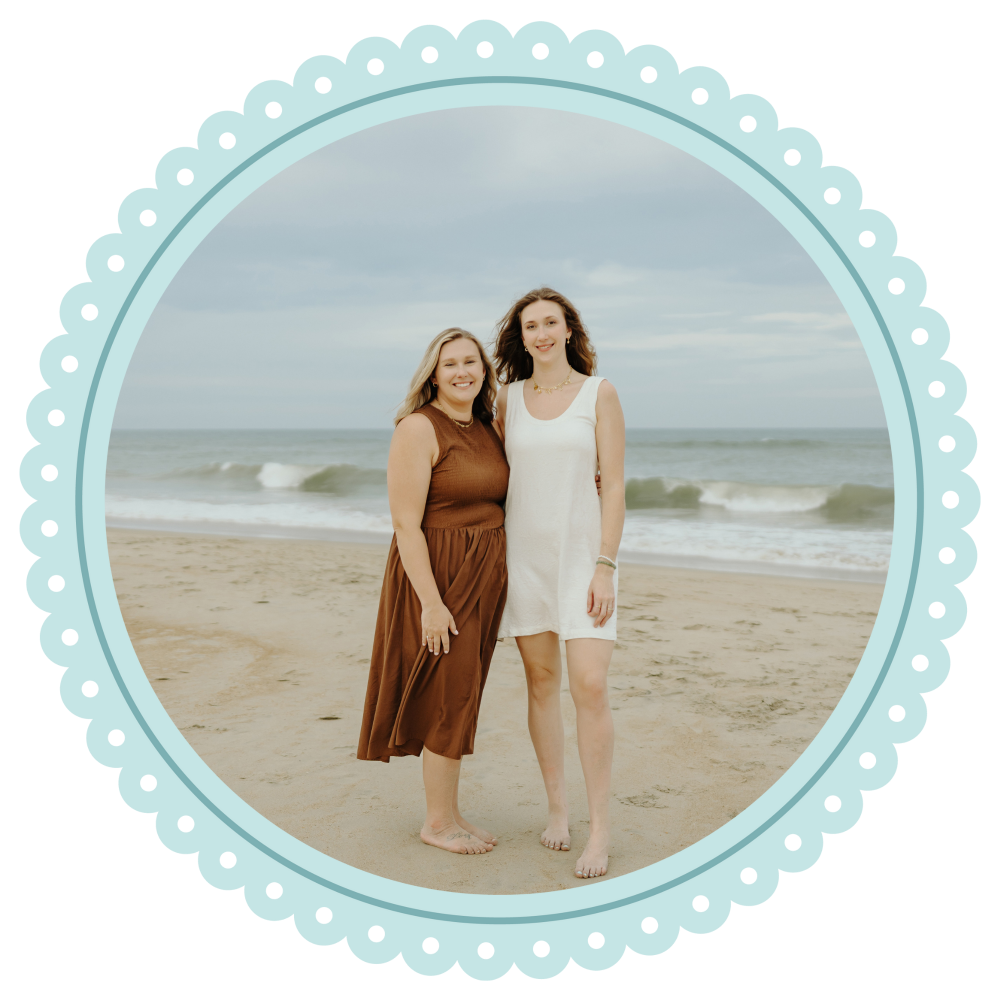 Two women standing on a beach with a decorative blue border.
