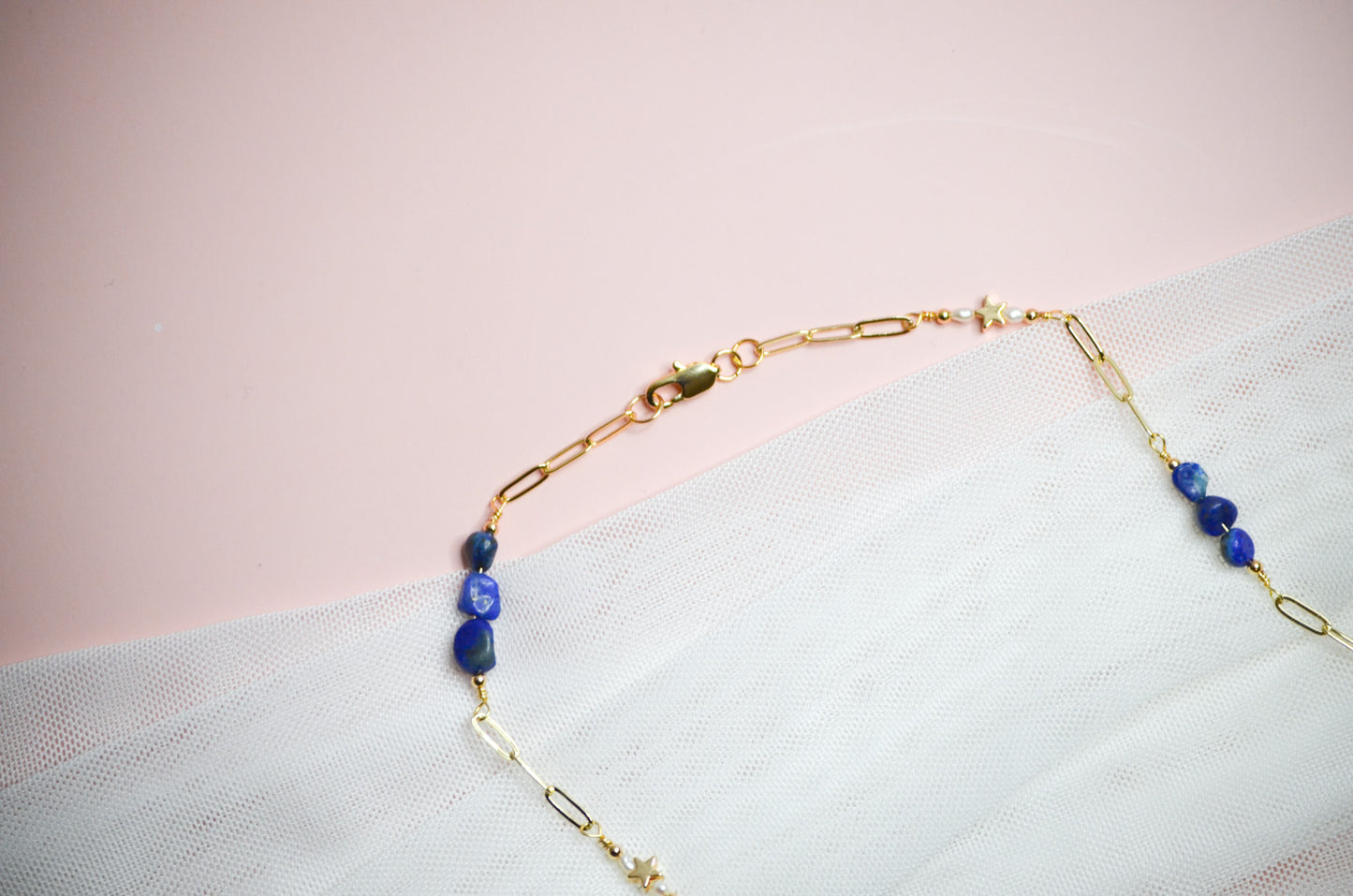Gold necklace with blue beads on a light pink background
