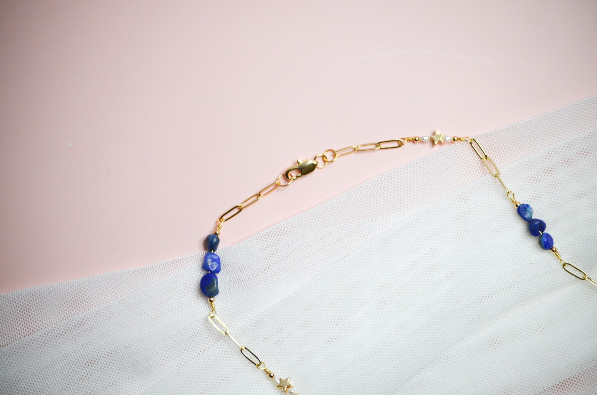 Gold necklace with blue beads on a light pink background