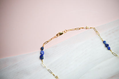 Gold necklace with blue beads on a light pink background