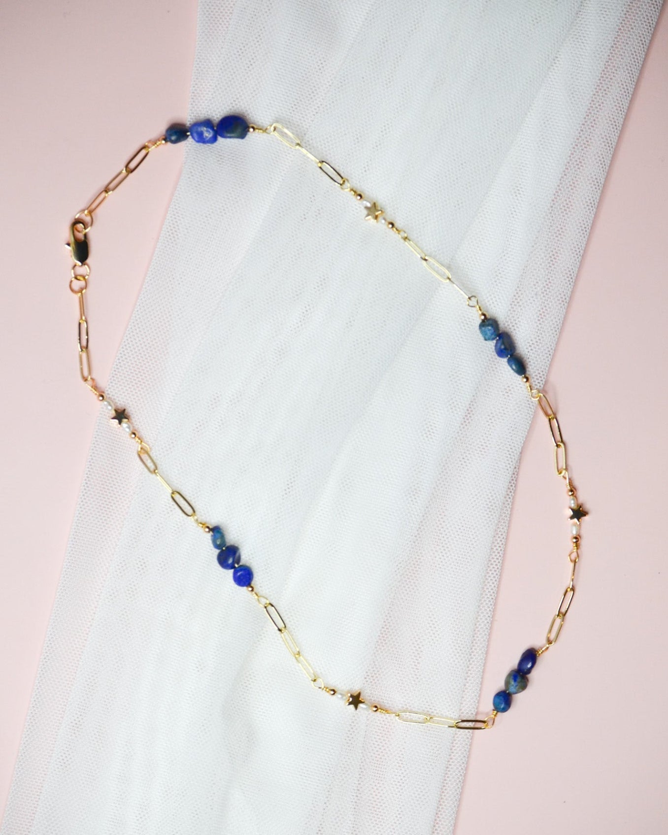 Gold chain necklace with blue lapis lazuli and gold star beads on a white fabric background