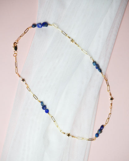 Gold chain necklace with blue lapis lazuli and gold star beads on a white fabric background